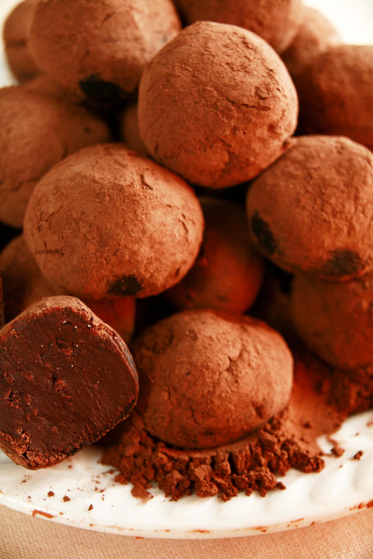 Close up view of a small white plate piled with homemade truffles.  They're made from dark chocolate, and are rolled in cocoa powder.