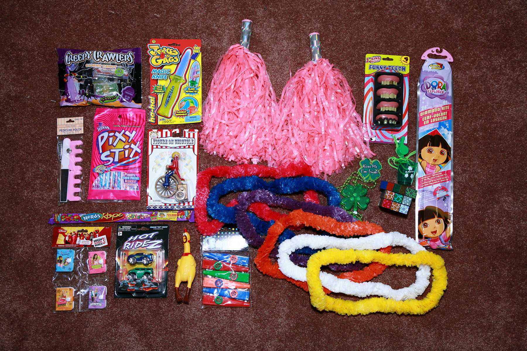 An assortment of candies and random toys - pinata stuffing - is shown spread out on a brown carpet.