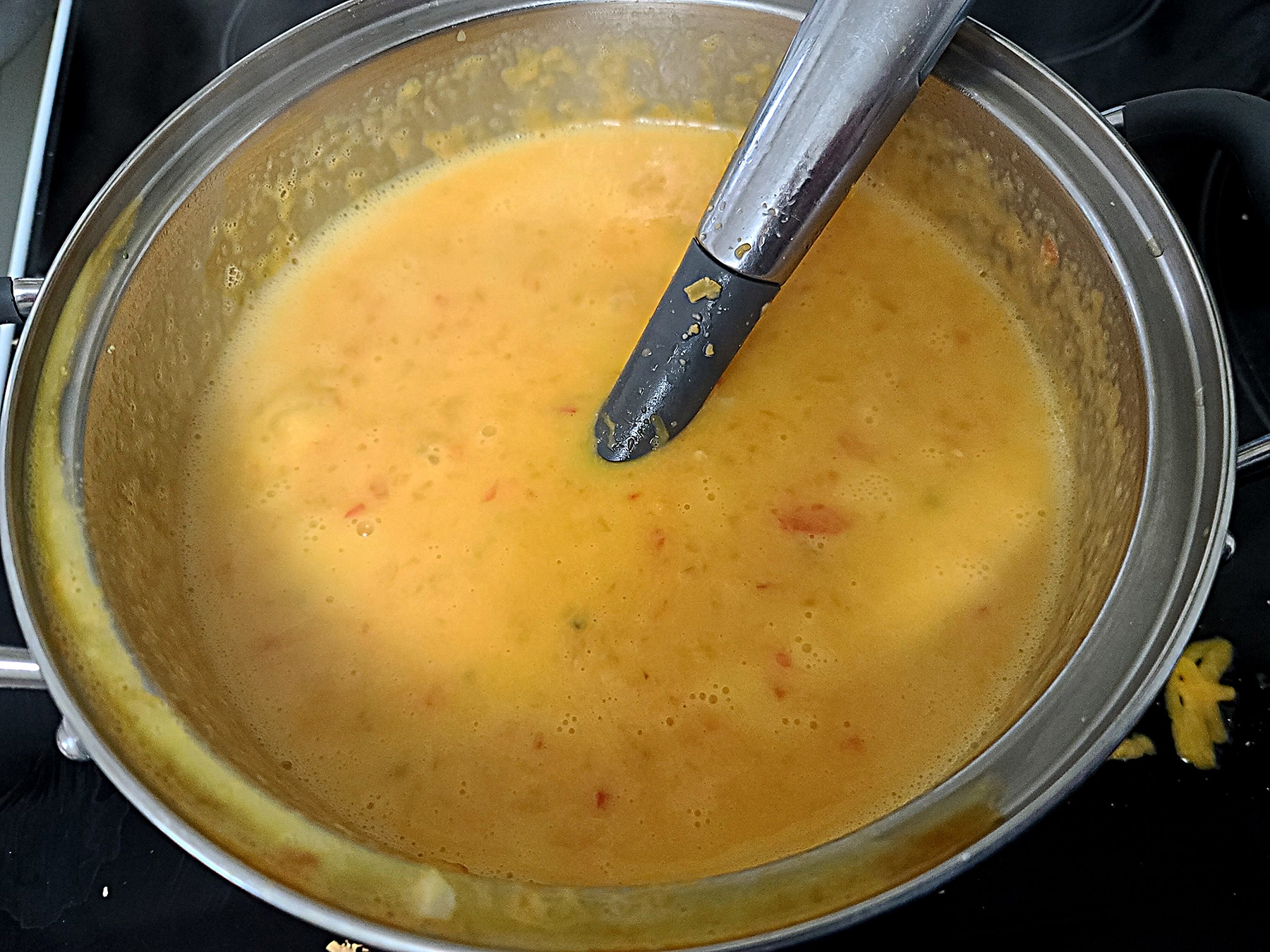 A pot of orange coloured cheese fondue, with small bits of peppers throughout.