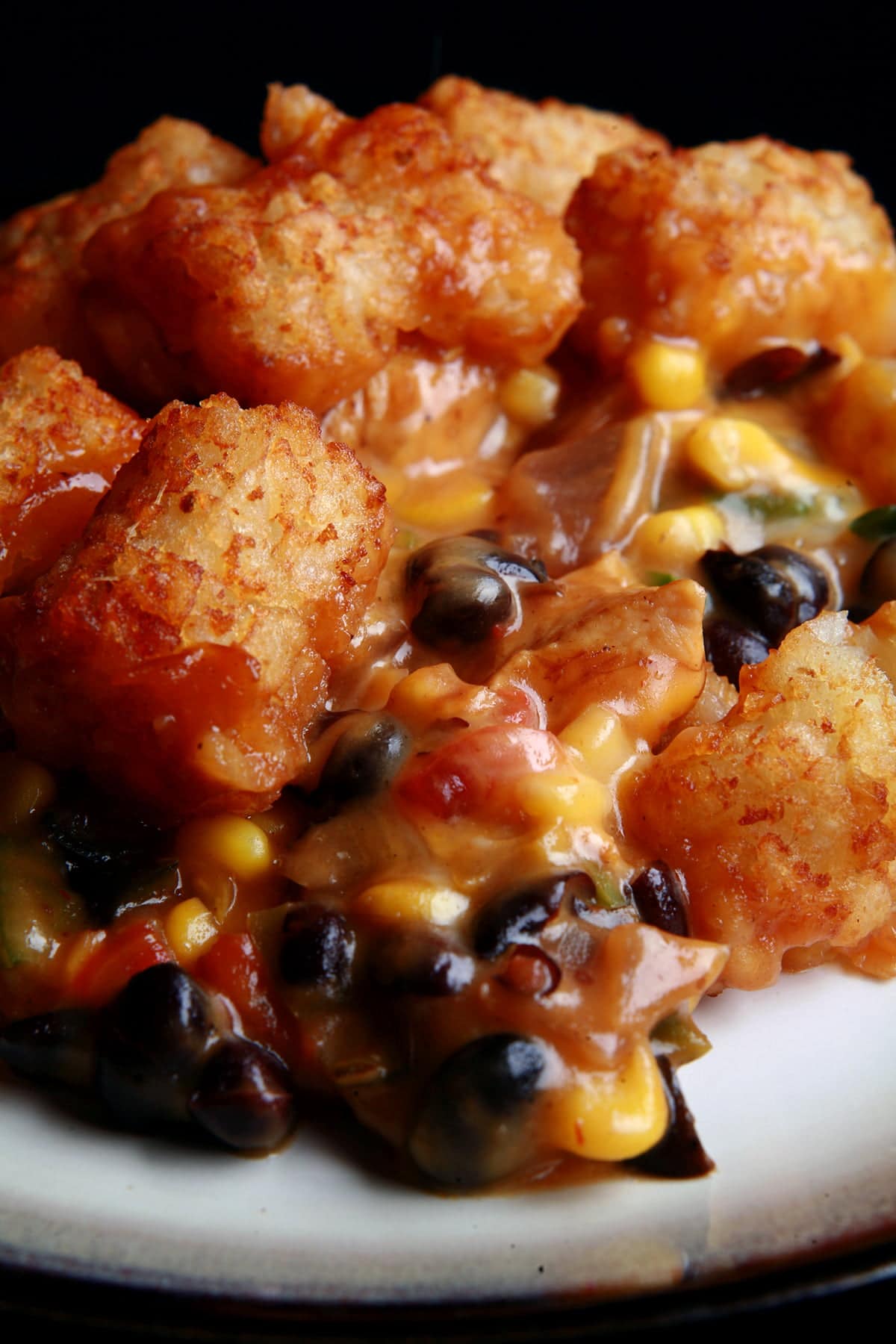 A close up view of a serving of southwest hot dish. Chicken, black beans, salsa, cheese sauce are visible, with crispy tater tots on top.