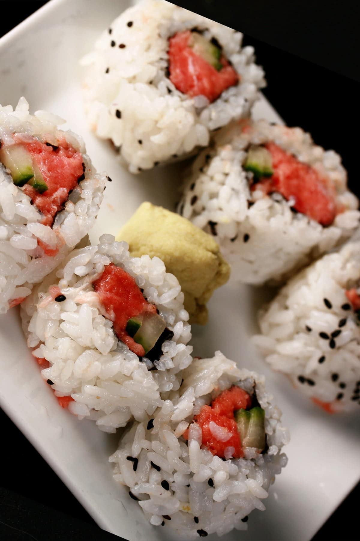 6 pieces of spicy tuna maki are arranged on a white plate, with a glob of wasabi in the middle.