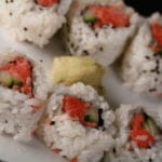 6 pieces of spicy tuna sushi roll are arranged on a white plate, with a glob of wasabi in the middle.