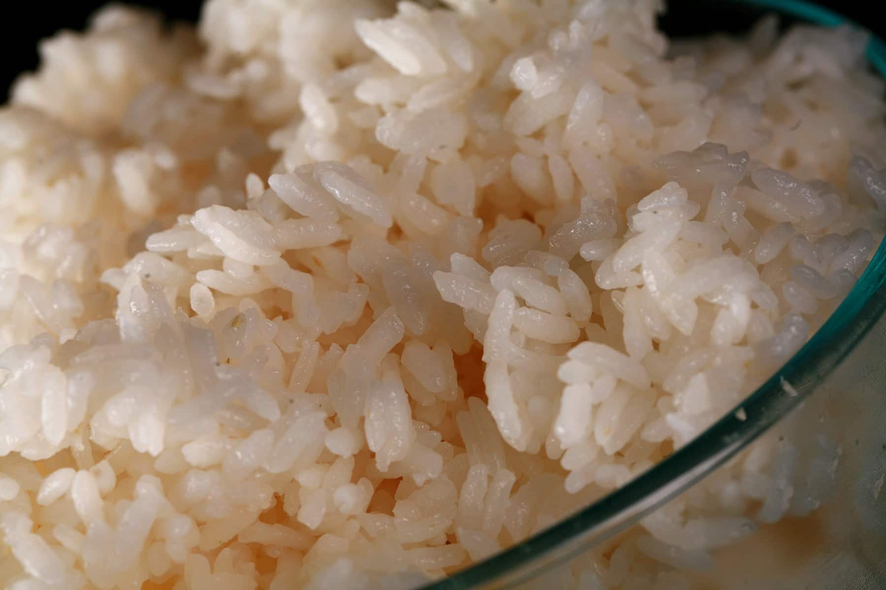 A glass bowl of sticky white rice against a black background