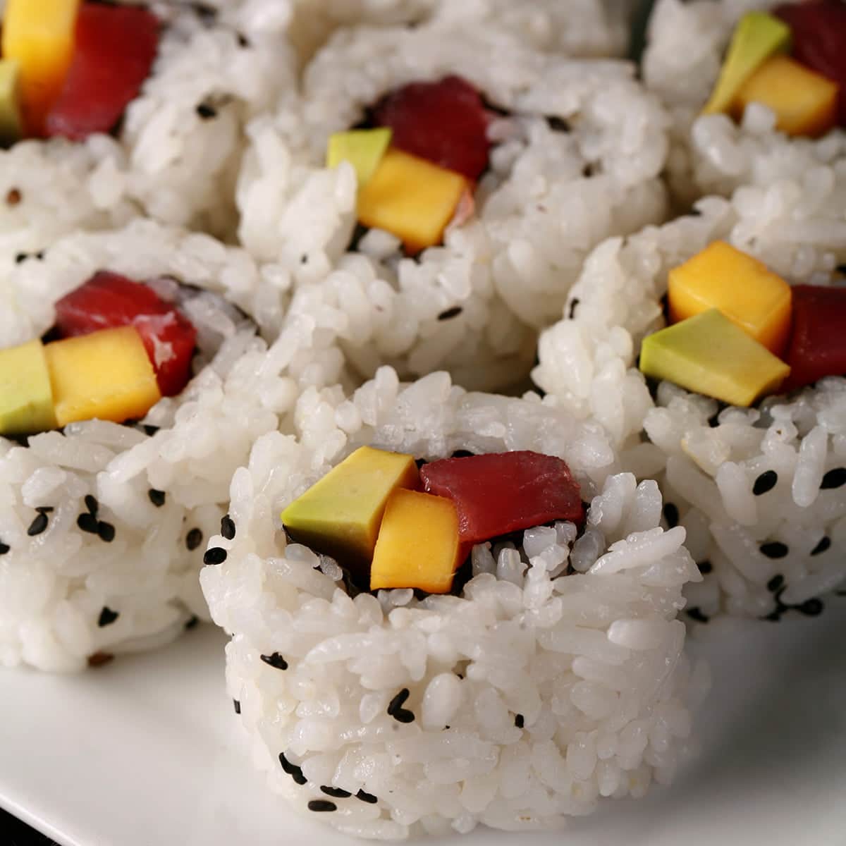 7 pieces of tuna avocado and mango sushi roll slices, on a small white plate.