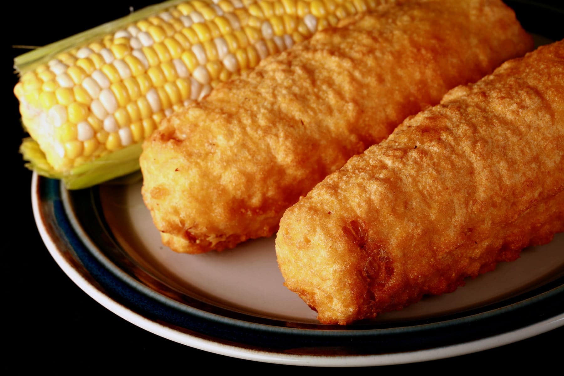3 cobs of corn - 1 fresh, 2 battered and deep fried - are lined up on a plate.