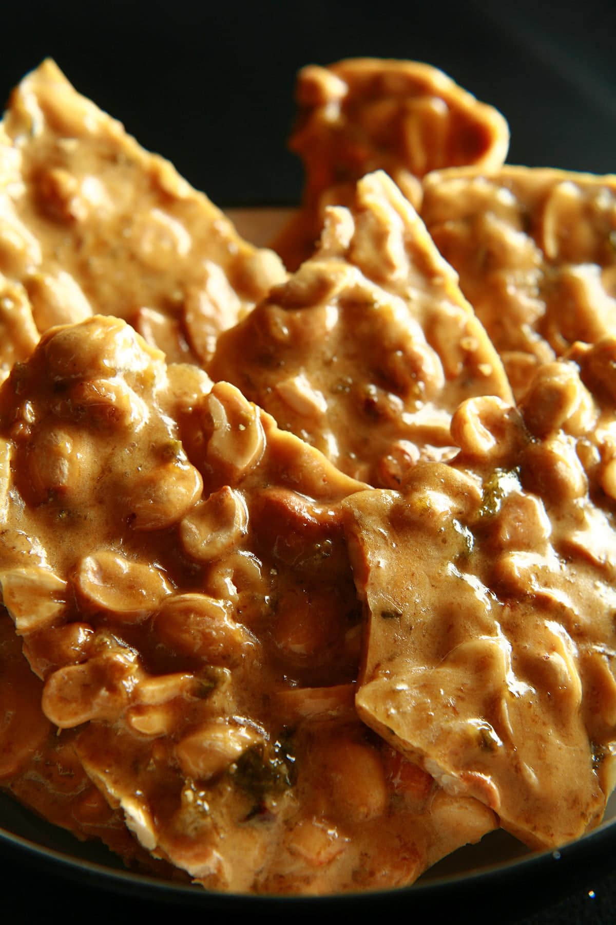 A close up view of peanut brittle with green flecks throughout - jalapeno pieces!