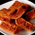 Chunks of deep amber coloured sponge toffee are piled on a small white plate.