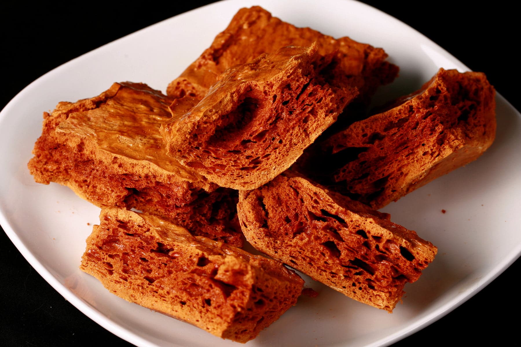 Chunks of deep amber coloured sponge toffee are piled on a small white plate.