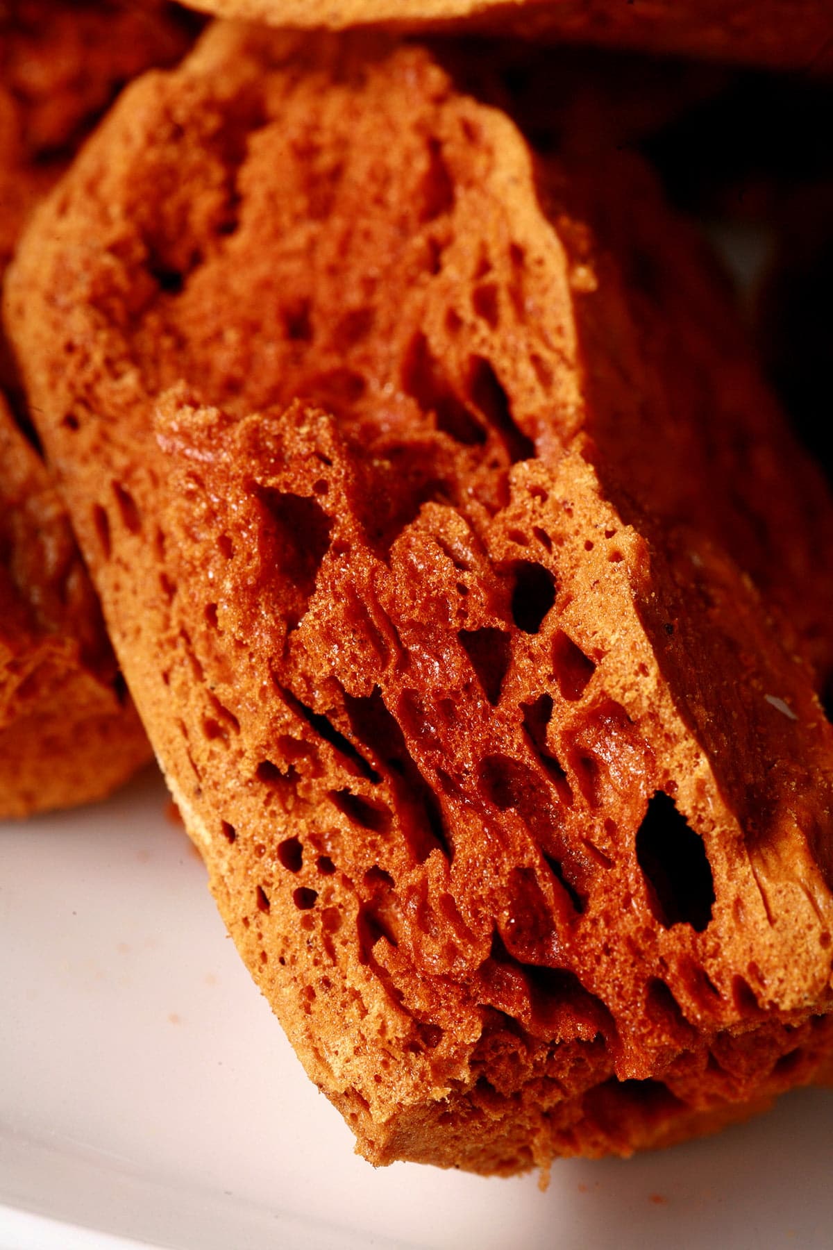 Chunks of deep amber coloured ginger-molasses sponge toffee are piled on a small white plate.