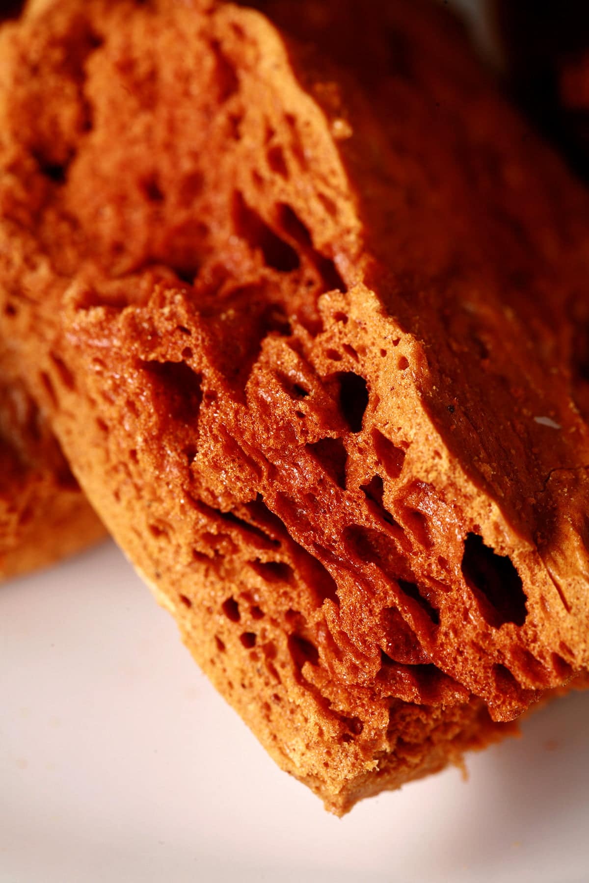 Chunks of deep amber coloured ginger-molasses sponge toffee are piled on a small white plate.