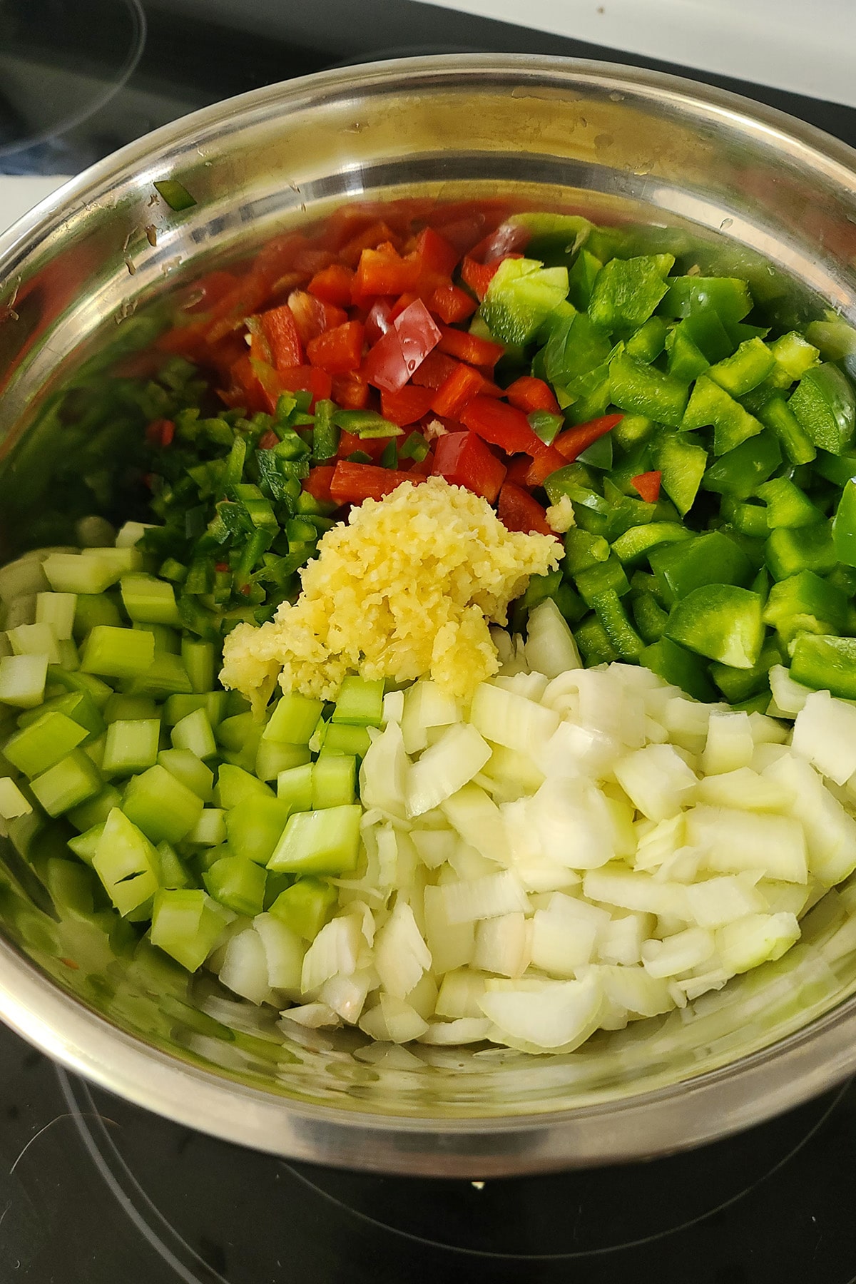 A large mixing bowl with chopped peppers, onions, celery, and garlic in it.