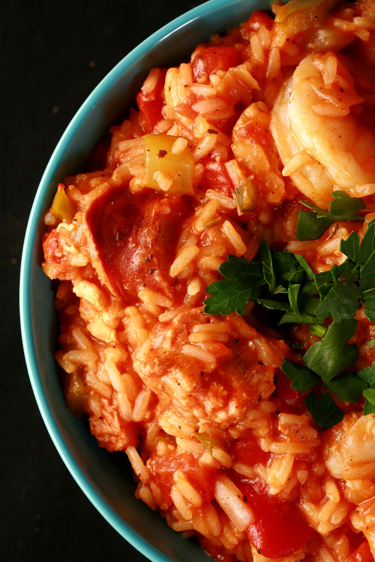 Chicken, shrimp, and sausage jambalaya, in a blue bowl. It is topped with chopped parsley.