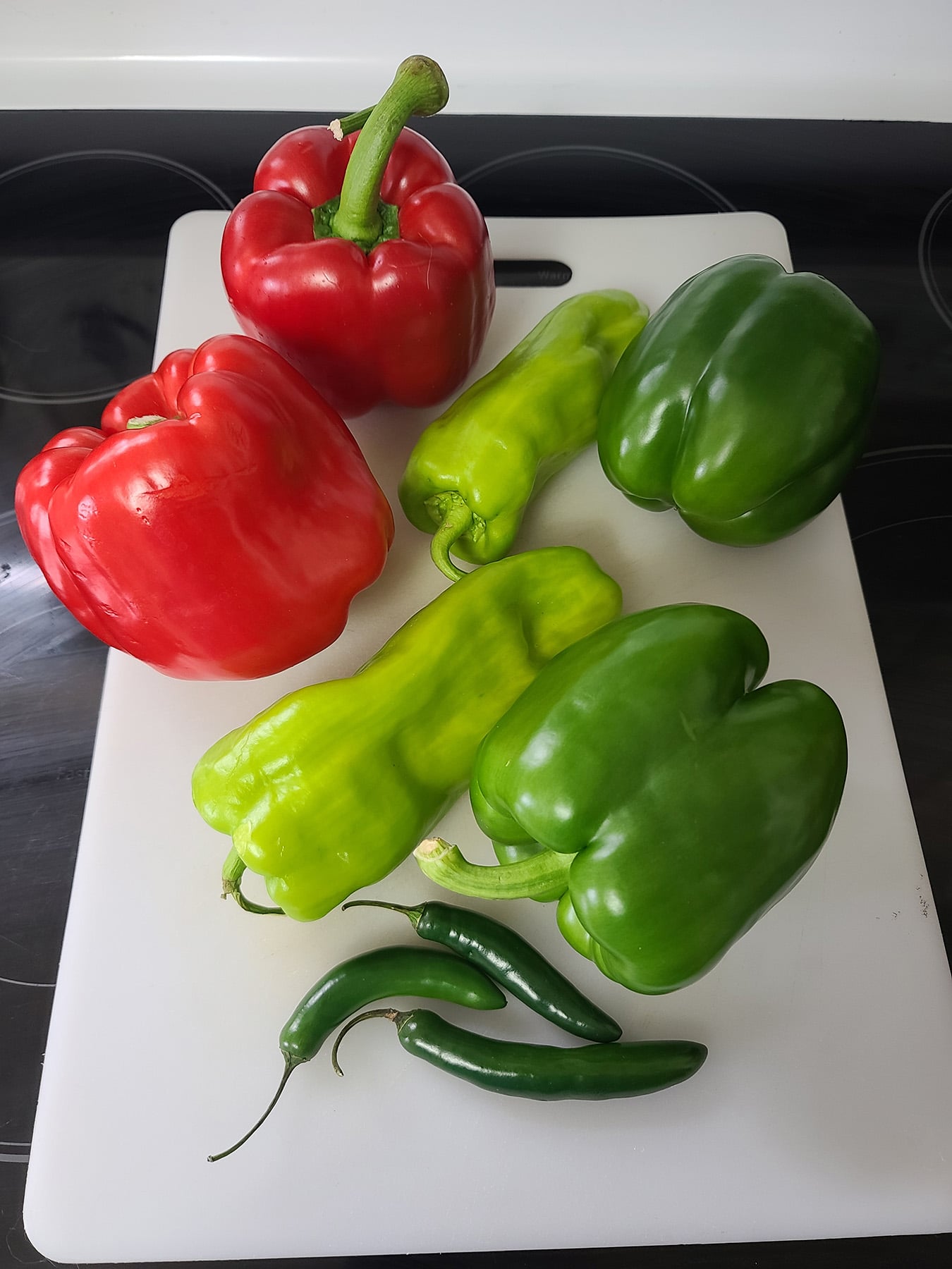 Several red and green peppers on a cutting board.