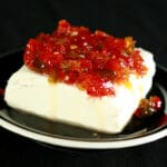 A mound of pepper jelly on a chunk of cream cheese on a small black plate.