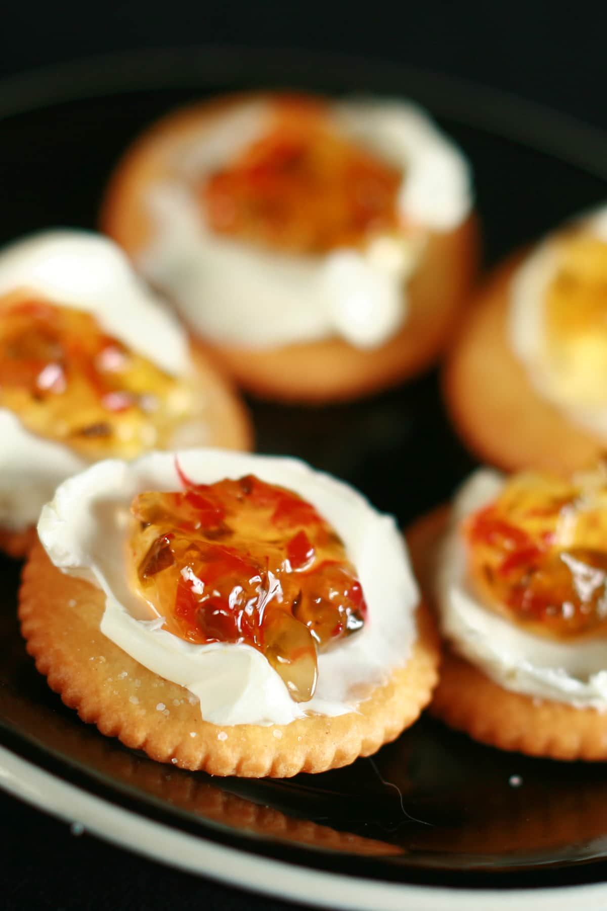 A black plate with Ritz crackers. They've been topped with a smear of cream cheese, and a dollop of pepper jelly.