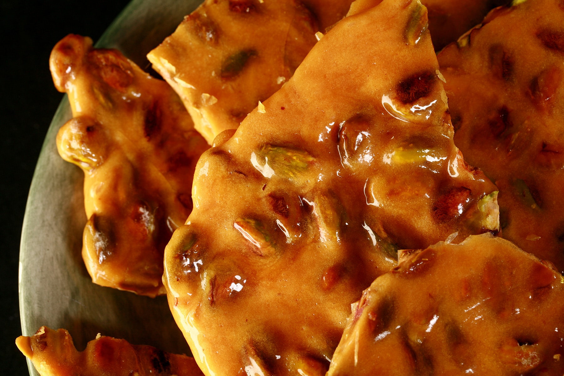 Chunks of pistachio brittle on a green plate.