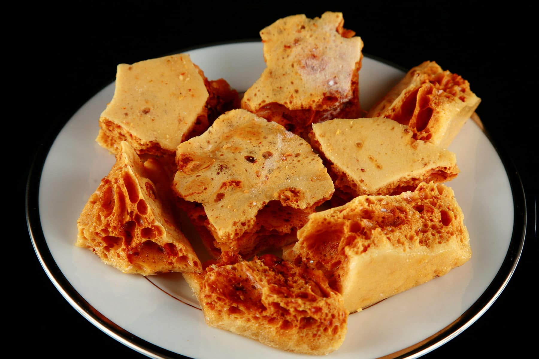Close up view of a plate of golden sponge toffee chunks.