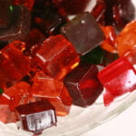 A glass bowl full of homemade jolly rancher candy -clear square shaped hard candy in orange, red, green, and purple