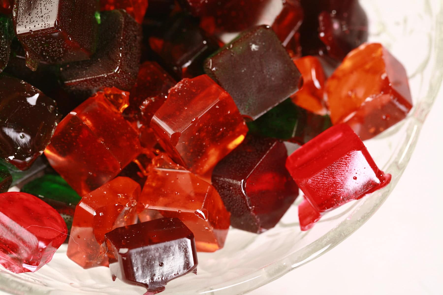 A glass bowl full of homemade jolly rancher candy -clear square shaped hard candy in orange, red, green, and purple