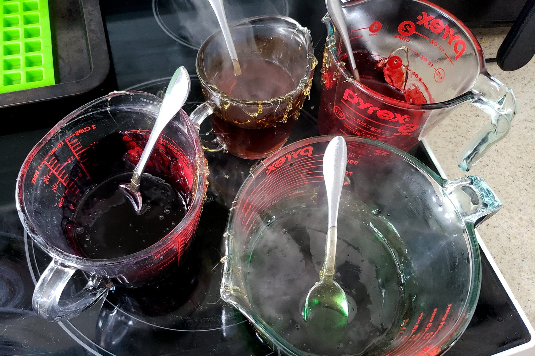 4 glass measuring cups are shown with small amounts of coloured liquid in each.