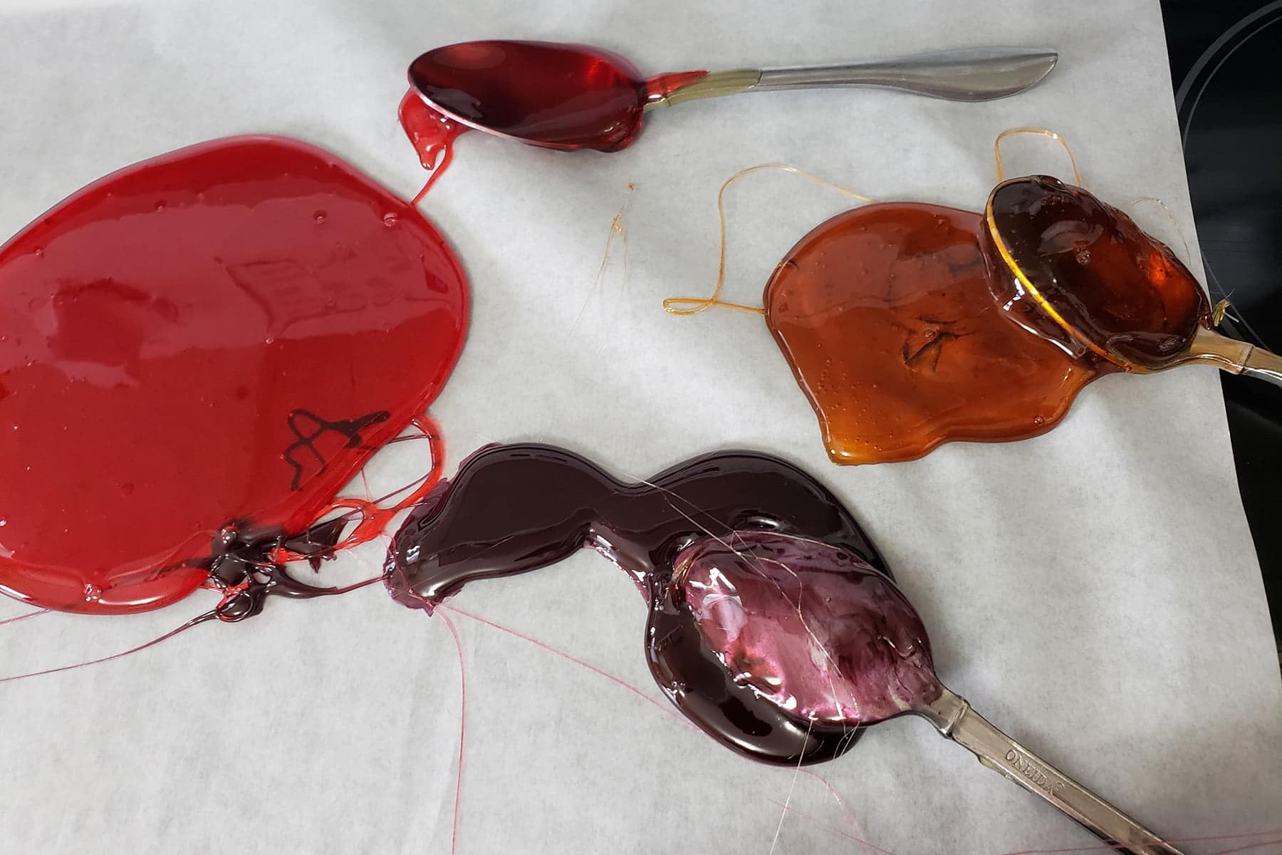 3 blobs of hard candy are shown on parchment paper, along with candy coated spoons.