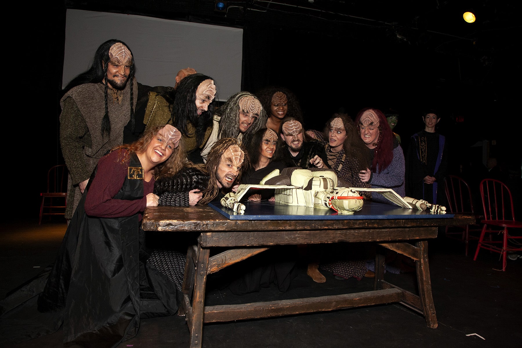 A group of Klingons gathered around a table. on the table is the Klingon ship cake.