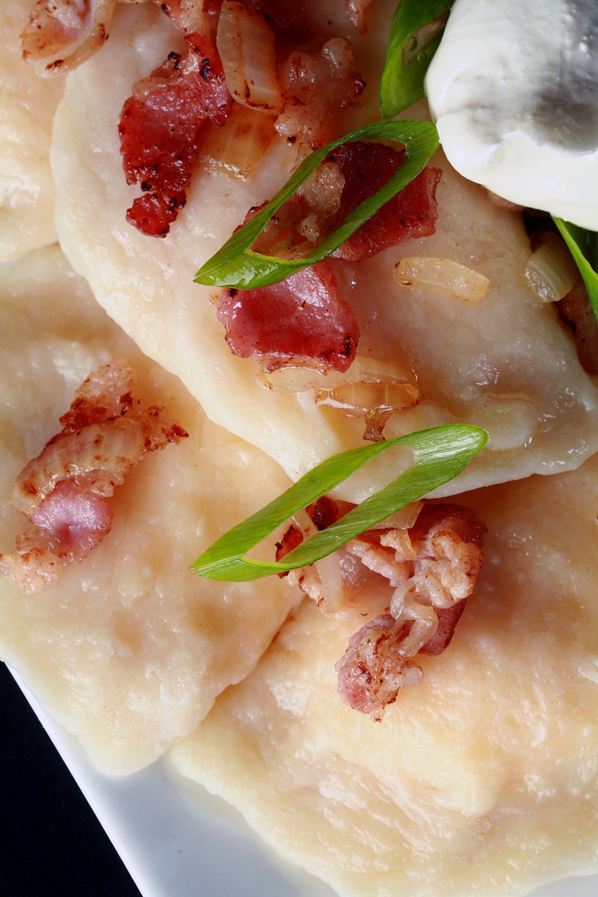 A plate of homemade pierogi with bacon, green onions, and sour cream.