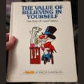 A hand holds up a copy of The Value of Believing in Yourself: The Story of Louis Pasteur.