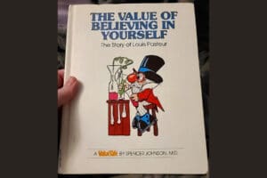 A hand holds up a copy of The Value of Believing in Yourself: The Story of Louis Pasteur.