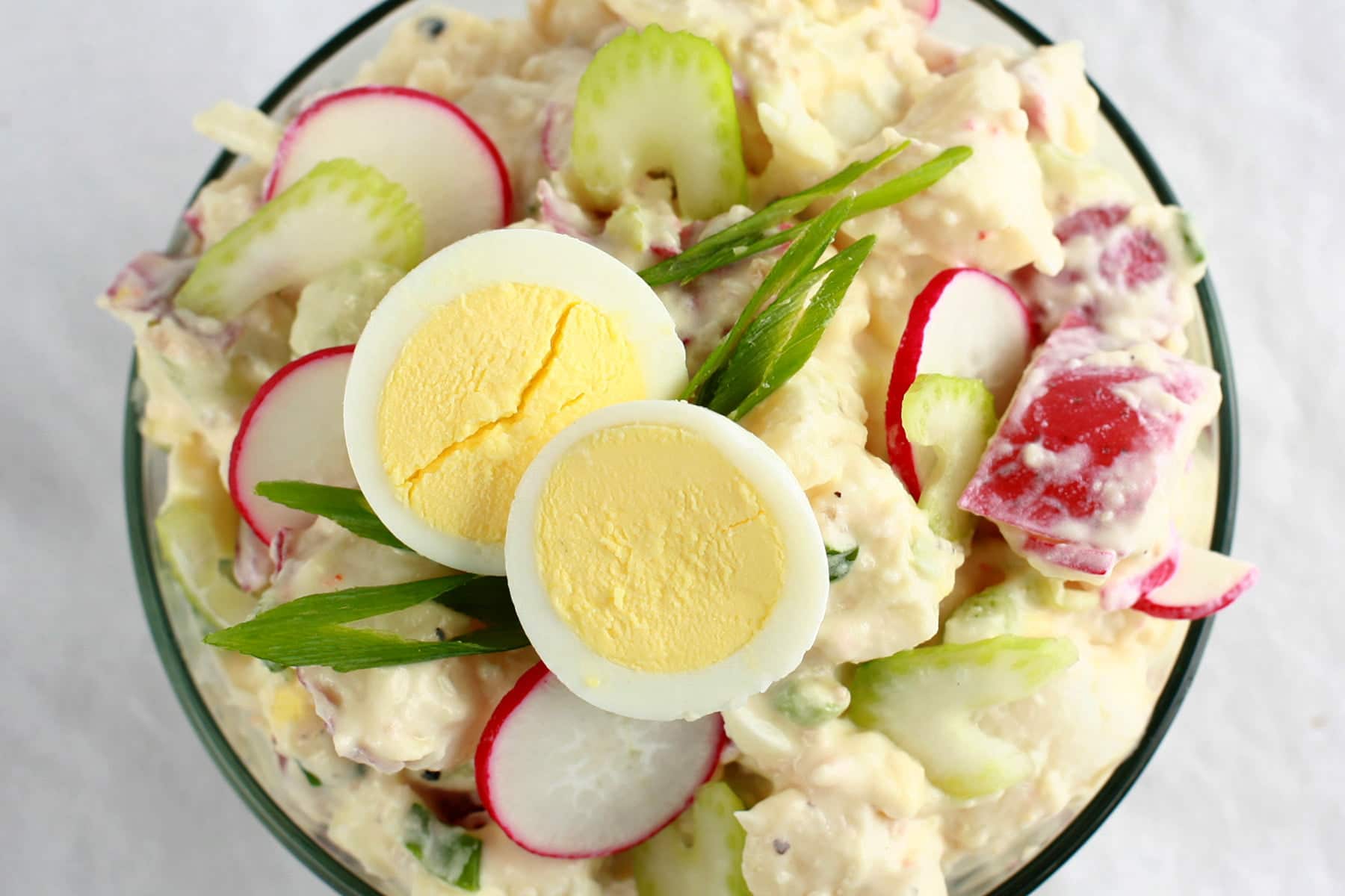 A bowl of Gramma's Potato Salad - a creamy potato salad with slices of celery, radish, green onion, and hardboiled egg visible.