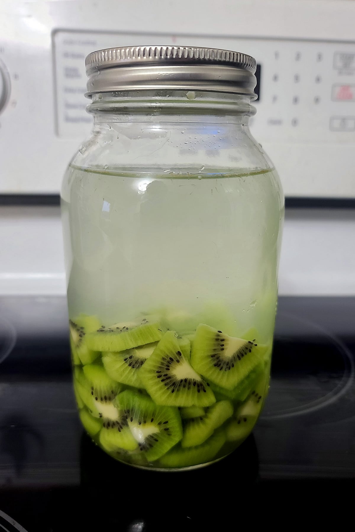 Chopped kiwifruit in a large mason jar with vodka in it.