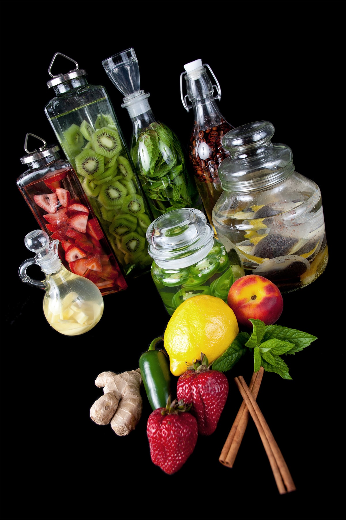 Several glass jars filled with different ingredients steeping in vodka.  Cinnamon, coffee, strawberries, lemon, ginger, iced tea, and more.
