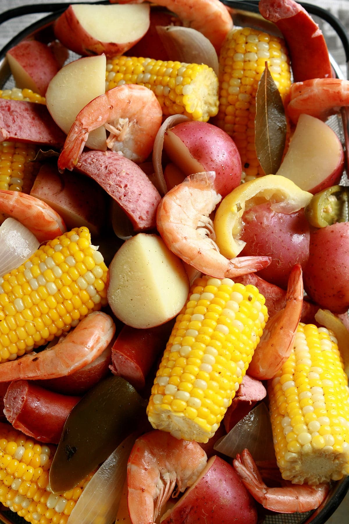 A close up view of a batch of low country boil: Red potatoes, corn on the cob, shrimp, and sausage.