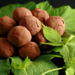 A mound of hop flavored dark chocolate truffles rests on a pile of hop leaves and hop bines.