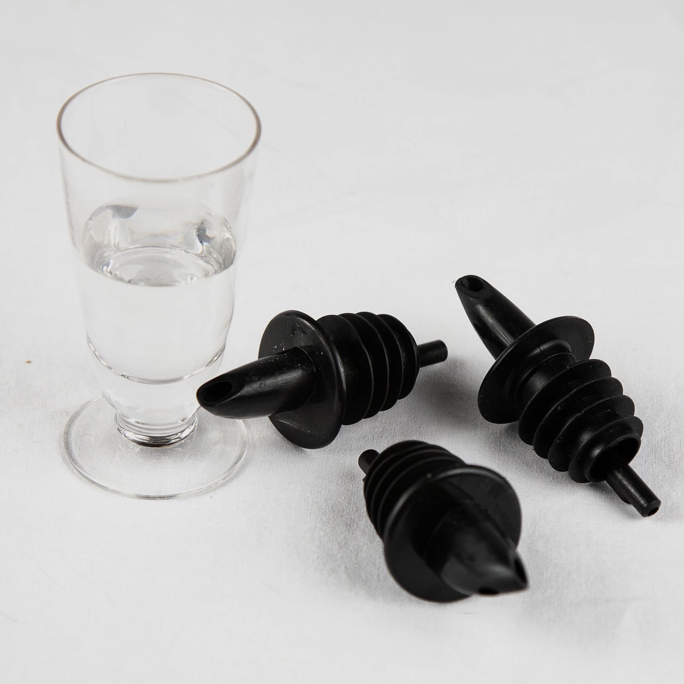 A shot glass half-filled with a clear liqueur, and 3 black pour spouts next to it.