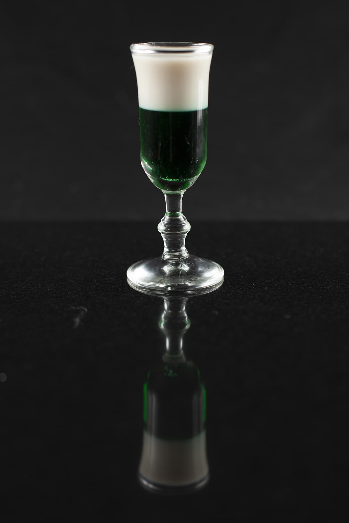 A green and black layered shot cocktail in a stemmed glass.