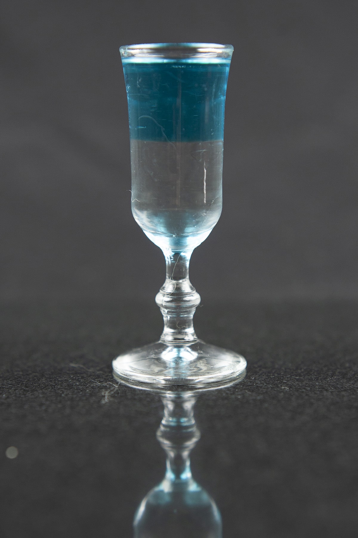 A clear and light blue layered shooter in a stemmed shot glass.