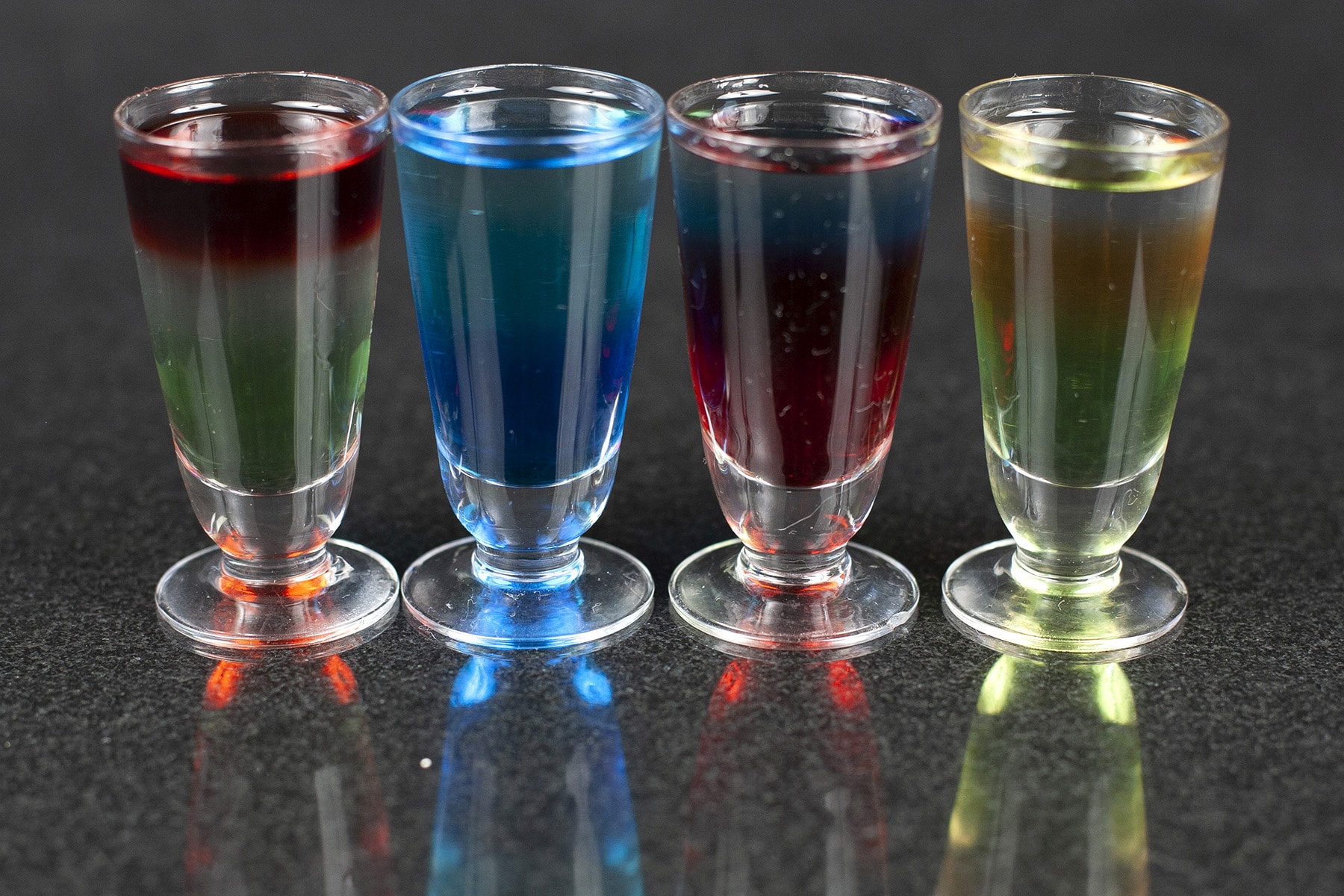 A line of multicoloured layered shooters in stemmed shot glasses.