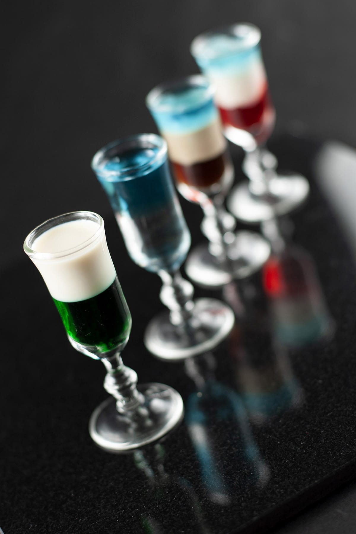 A line of multicoloured layered shooters in stemmed shot glasses.