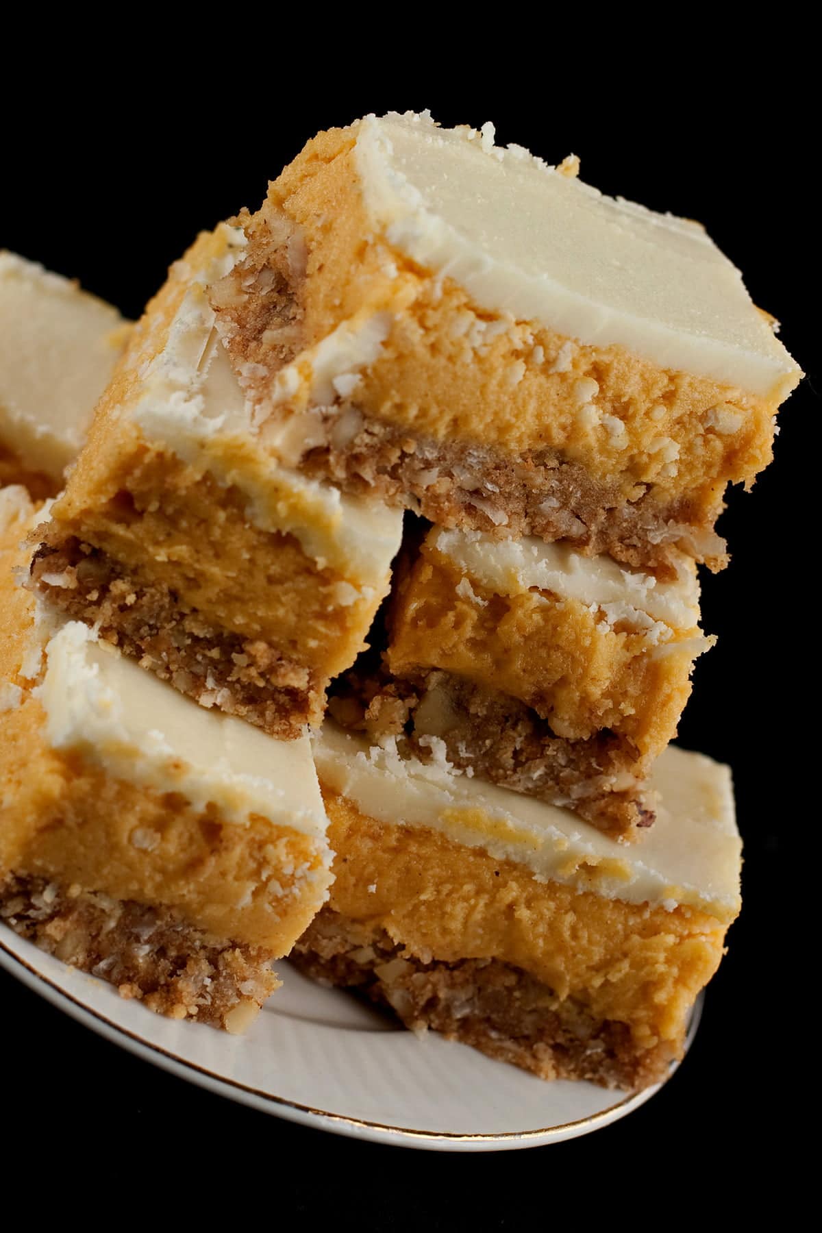 A plate of Pumpkin Nanaimo Bars - 3 layered bars. The bottom layer is a graham cookie coloured base, the middle is an orange - pumpkin - buttercream, and it is topped off with white chocolate gamache.