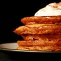 A tall stack of pumpkin spiced pancakes, topped with whipped cream and cinnamon.