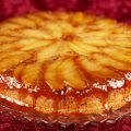 An apple upside down cake, with caramel dripping down from the top edge. It's against a burgundy fabric background.
