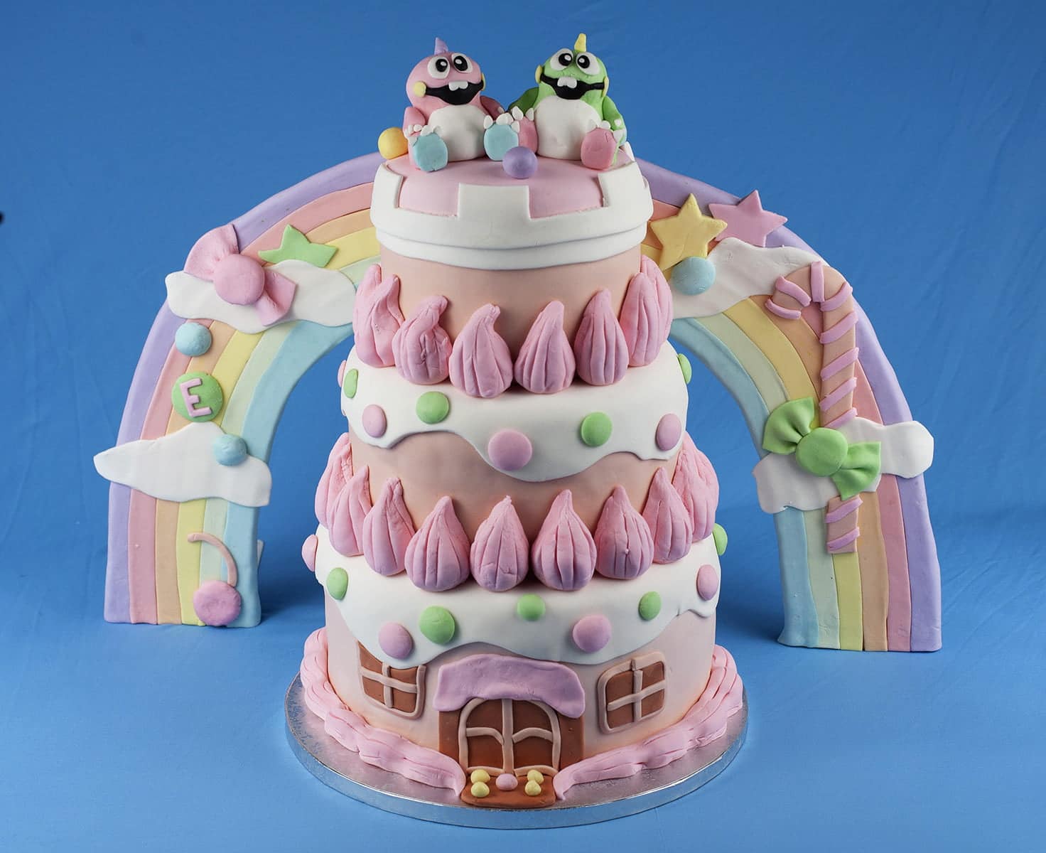 Detailed shots of a Bubble Bobble themed wedding cake. It's 3 tiers of pinks, whites, and pastel colours, "candy", cartoon dinosaurs, and more.