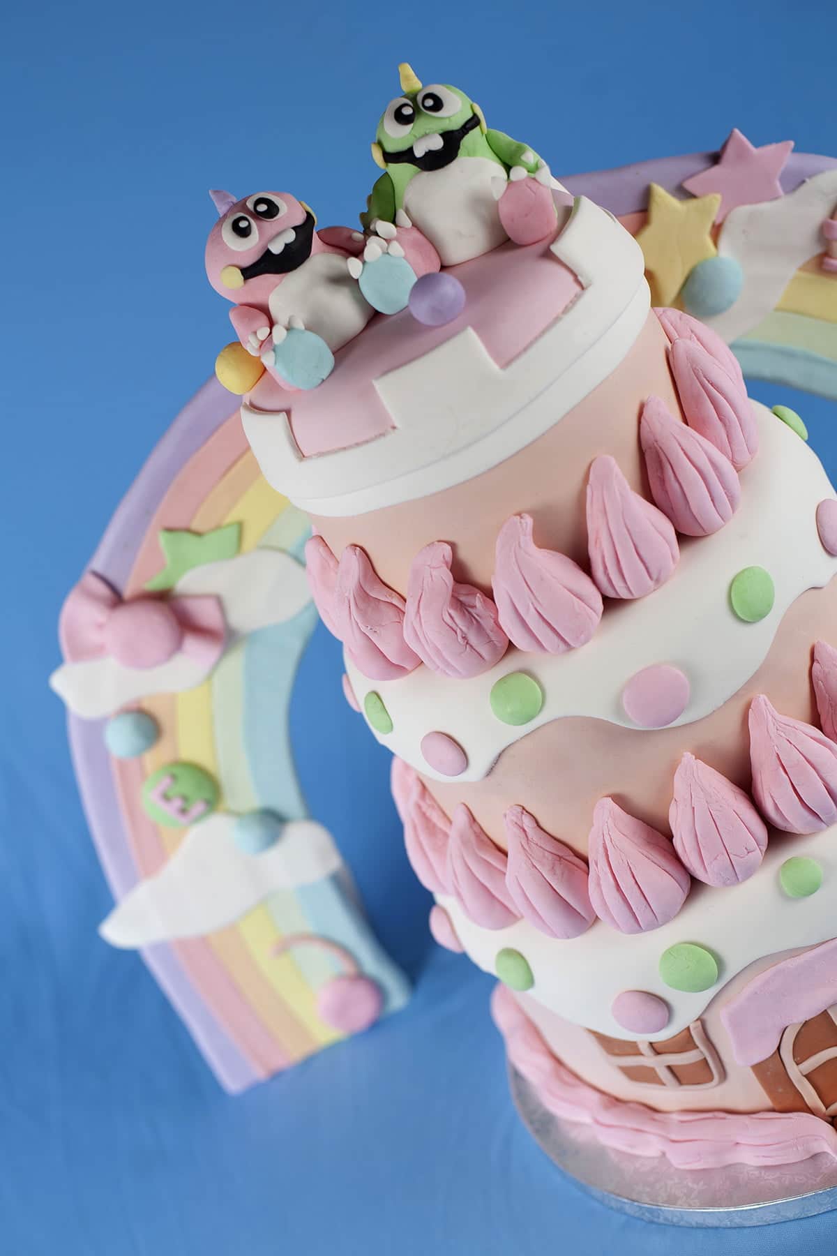 Detailed shots of a Bubble Bobble themed wedding cake. It's 3 tiers of pinks, whites, and pastel colours, "candy", cartoon dinosaurs, and more.