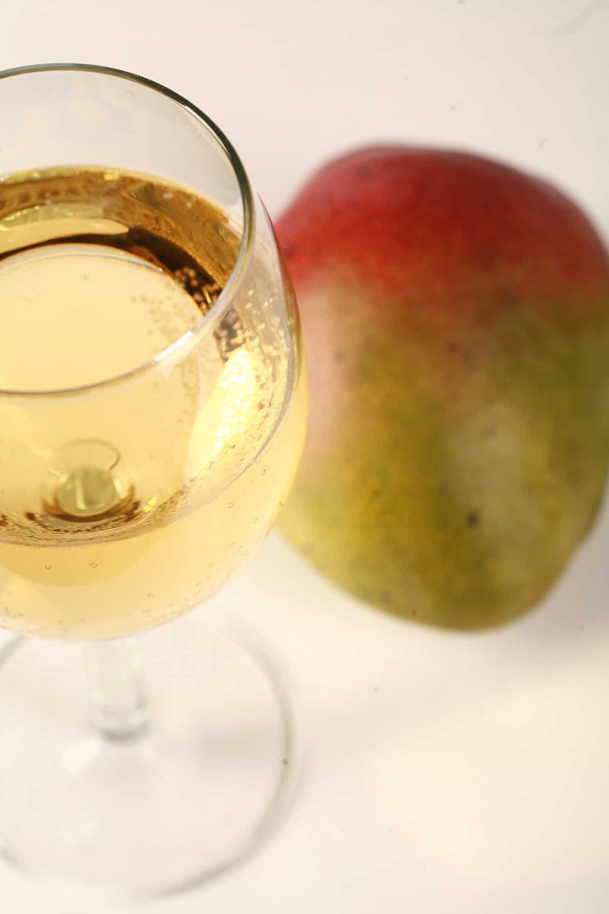 A glass of straw coloured wine is pictured next to a whole mango.
