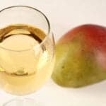 A glass of straw coloured wine is pictured next to a whole mango.