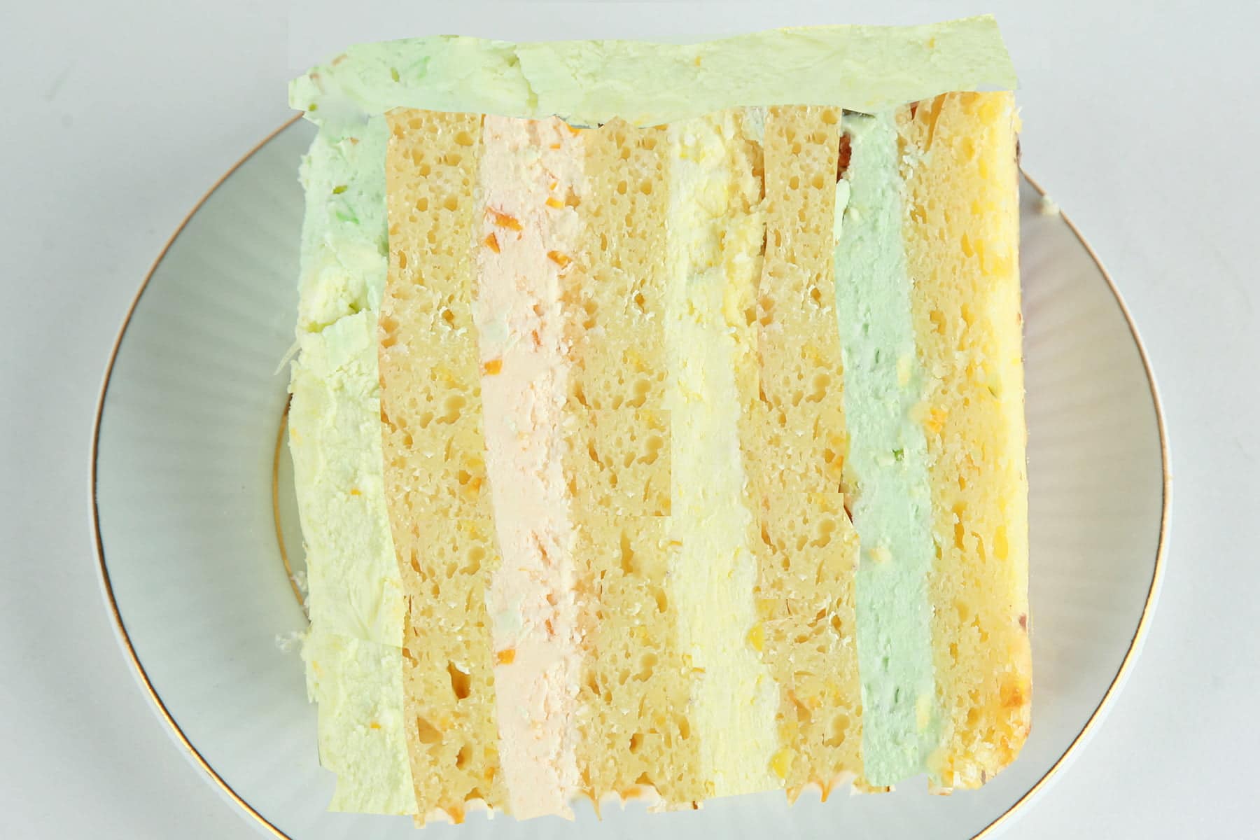 A slice of citrus splendor cake on a plate. 4 layers of a yellow citrus cake, separated by orange, lemon, and lime buttercream layers.