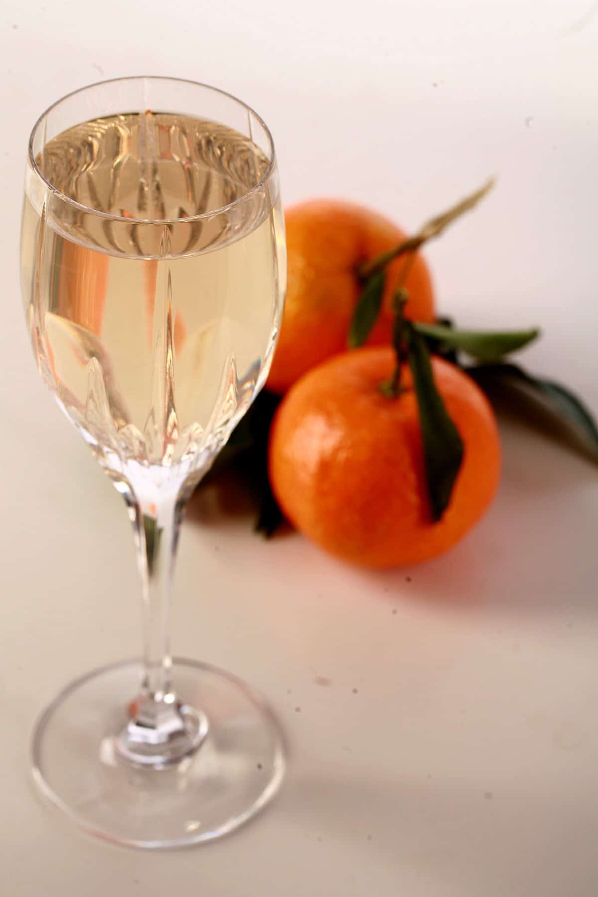 A glass of clementine mead is pictured with two clemetines at the base.