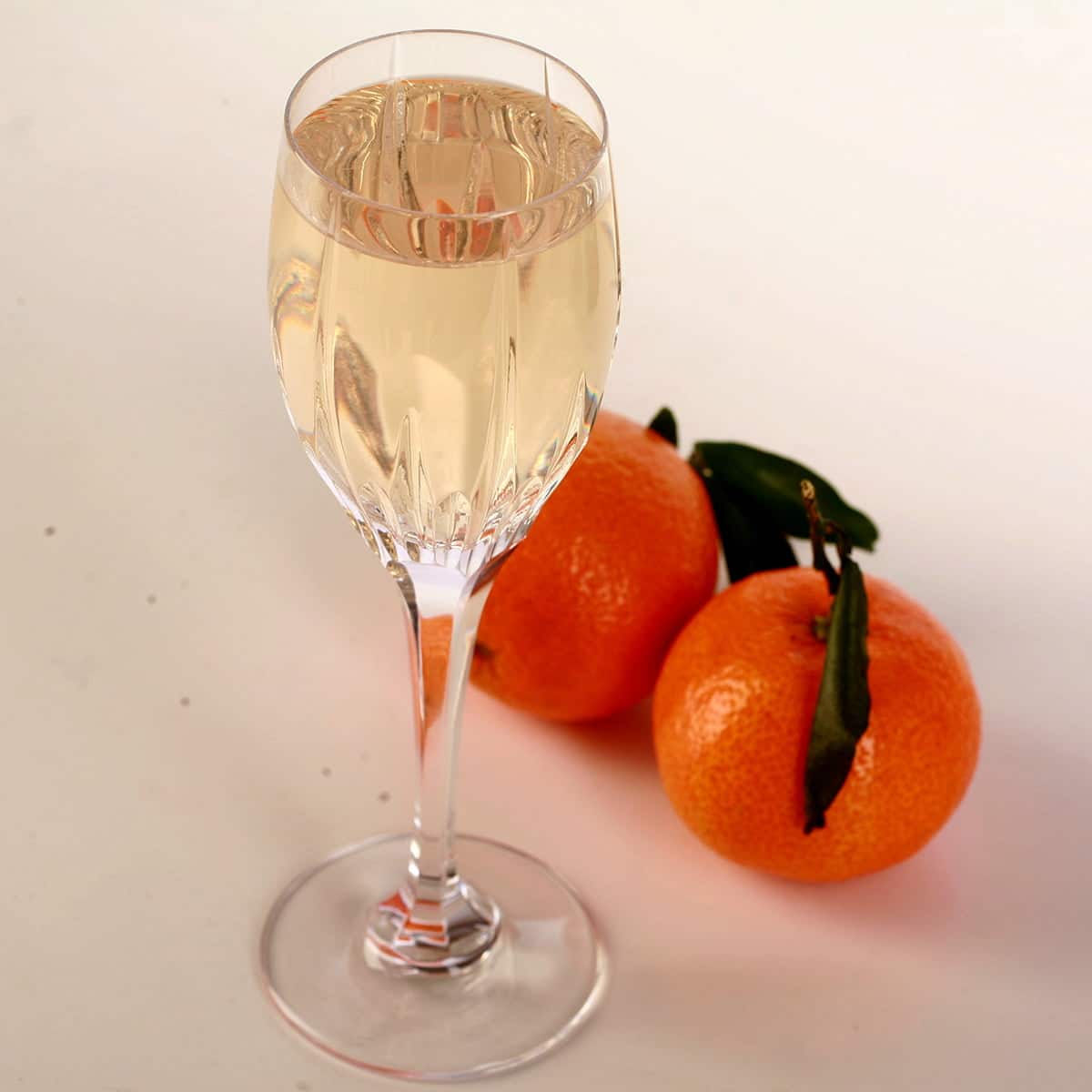 A glass of clementine mead is pictured with two clemetines at the base.