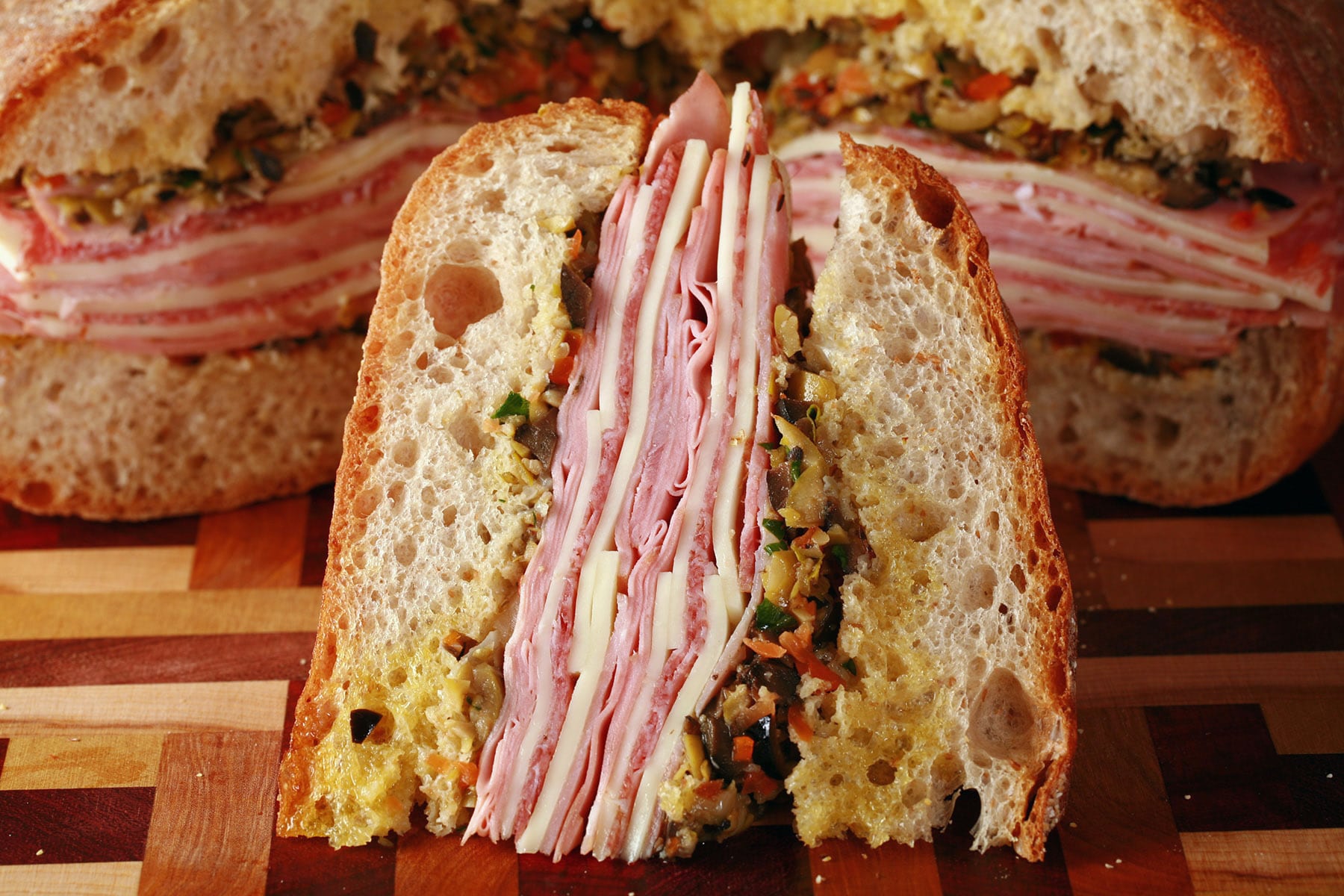 A close up view of a wedge of Muffaletta sandwich, with the remaining loaf behind it.